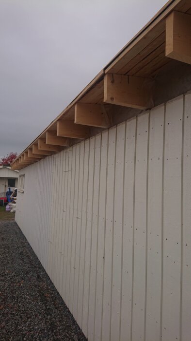 Träfasad med exponerade takreglar och en oskyddad takfot, visar konstruktionen utan inkapsling av springa under taket.