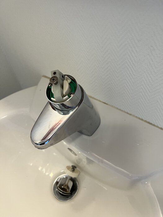 Bild på en läckande blandare från Gustavsberg i ett handfat, fotad utan överdel med insidan synlig.