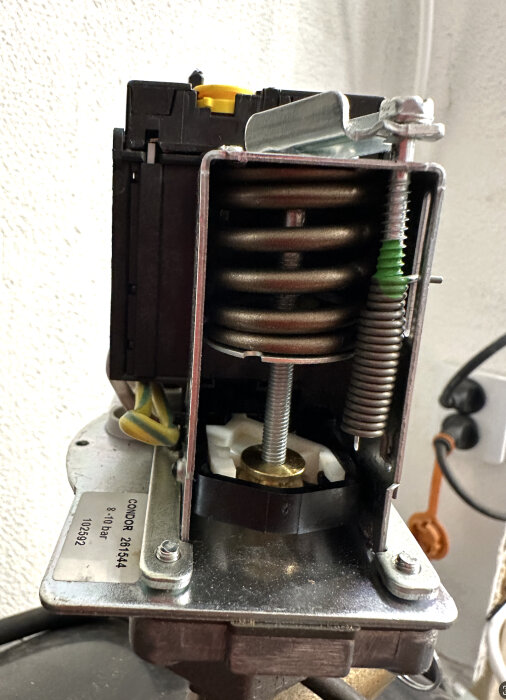 Närbild på relä med synlig fjäder och gul ratt för tryckavlastningsventilens inställning.