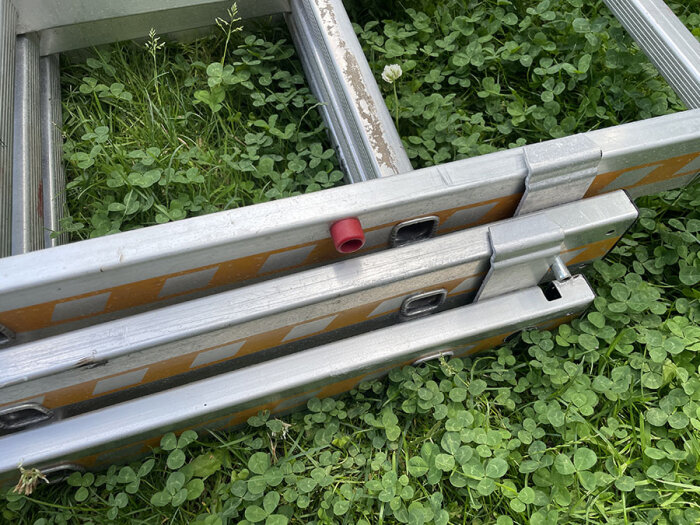 Hymerstege på gräs, delvis utdragen med tre sektioner. Synliga klämmor och en röd markering på ena sektionen.