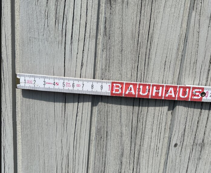 Måttband ligger mot en sliten träpanel som behöver repareras, assistans önskas kring utbyte av panelen under ett byggprojekt.