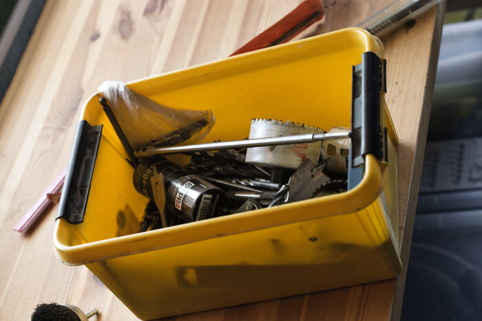 Gul låda fylld med olika borrverktyg, bland annat dosborr och plattborr, placerad på ett träbord.