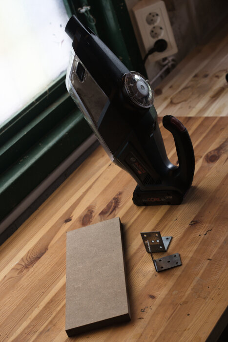 Minidammsugare från Bosch står på ett träbord bredvid en MDF-skiva och två vinkeljärn i en verkstadsmiljö.