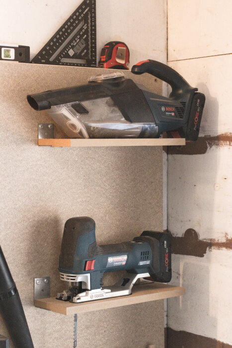 Hylla på vägg med en Bosch minidammsugare och sticksåg placerade på varsin hylla av MDF-fixering med vinkeljärn.