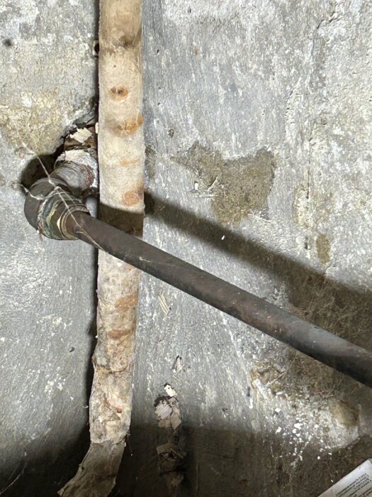 Dräneringshål i cementgolv med röranslutning och en del av en pump synlig.