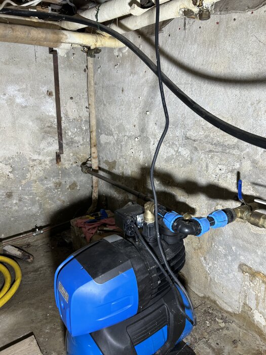 Dränkbar länspump i källare med anslutna rör och slangar mot grå betongvägg.