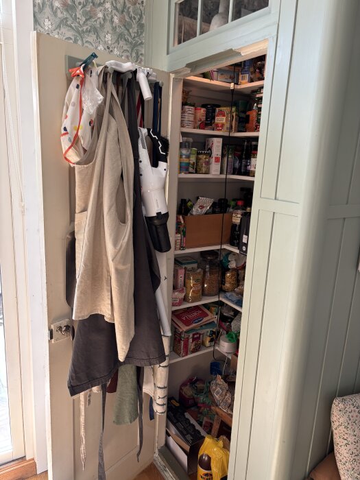 Skafferidörr med klädgalgar och förvaring, innehållande diverse matvaror. Regeln gjort av regelvirke och beläget vid ytterväggen.