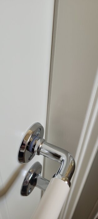 Kromat dörrhandtag på en vit toalettdörr som sluter tätt vid låset.