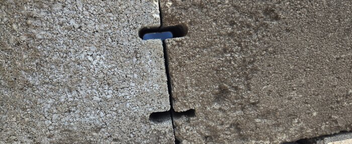Närbild av två grå betongblock med ovala hål där blå himmel syns genom, placerade sida vid sida med en springa mellan dem.