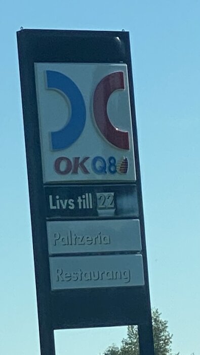 Skylt för OKQ8, med text om livsmedelsbutik öppen till kl 22 samt pizzeria och restaurang.