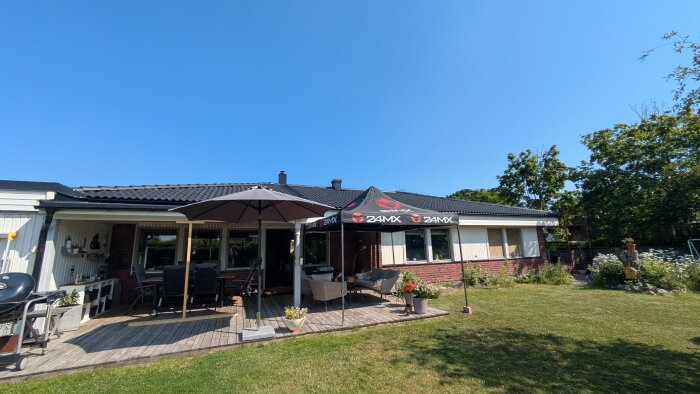 Hus med terrass under tillfällig pergola, parasoll och utemöbler.