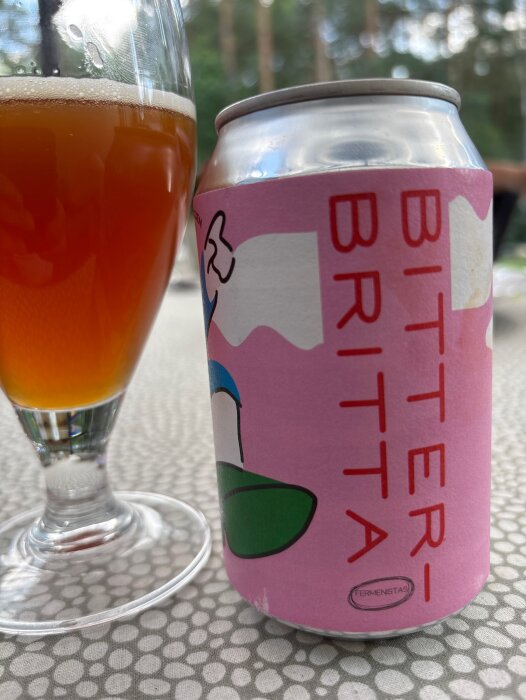 Burk och glas med Bitter Britta öl från Klackabacken på ett bord utomhus.