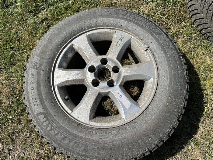 Vinterdäck från Volvo med femekrad fälg, liggande på gräs. Däckets märke är Michelin och det har synlig smuts kvar efter rengöring.
