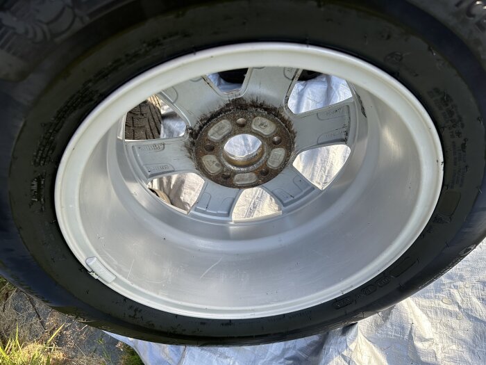 Rostig fälg till vinterhjul på en Volvo, under rengöring med spår av smuts och rost kvar, liggande på en presenning.