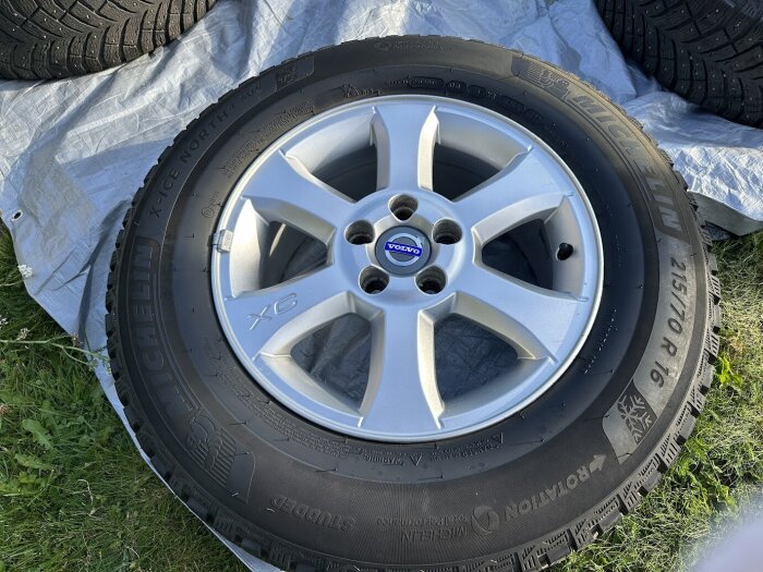 Volvo-vinterhjul med Michelin-däck och silverfärgad fälg ligger på gräs och presenning.