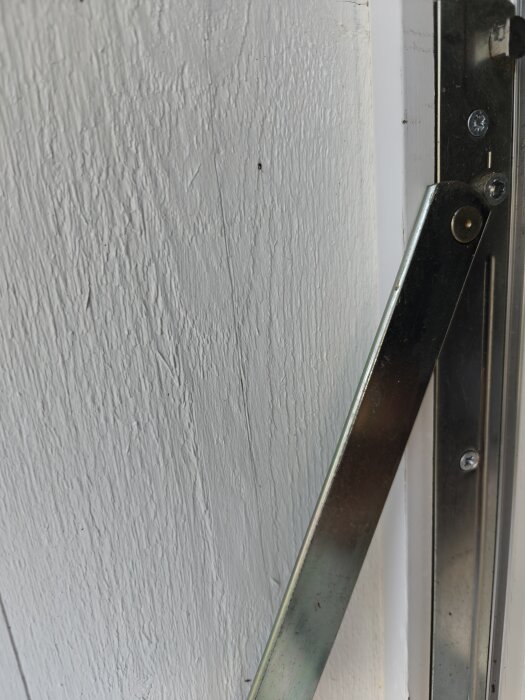 Metallgångjärn monterat på en vit träyta, del av ett fönster som inte är rakt.