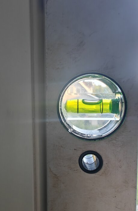 Närbild på ett vattenpass fäst på fönster, visar att det inte är i lod. En annan del av verktyget syns också som ett cirkulärt metallicrör.