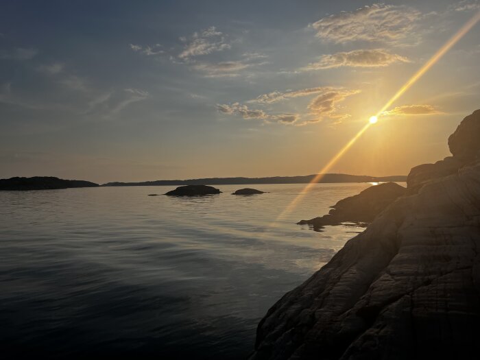 Solnedgång över stilla hav med klippor i förgrunden och några små öar i bakgrunden.