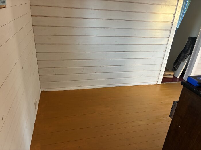 Nymålat rum med vita väggar och gult golv i linoljefärg.