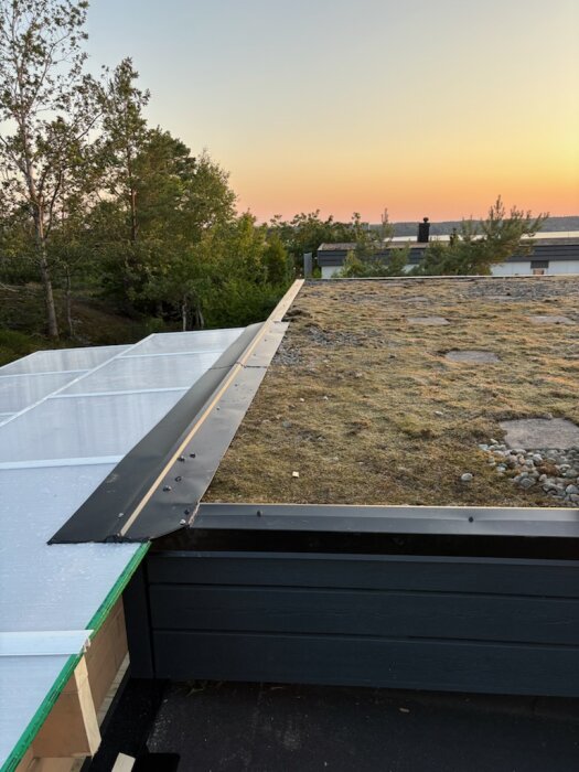 Platt tak med sedum och sten, fastmonterad plåt, buckla på kanalplast, solnedgång i bakgrunden.
