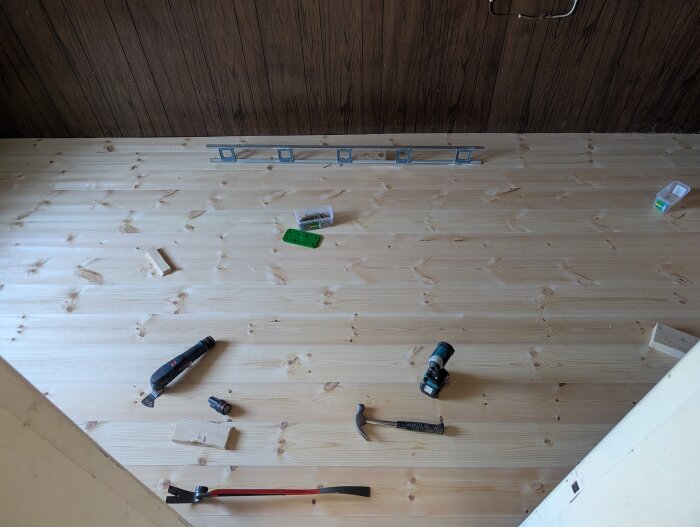 Nylagt trägolv med verktyg och byggmaterial som en hammare och borr på ytan.