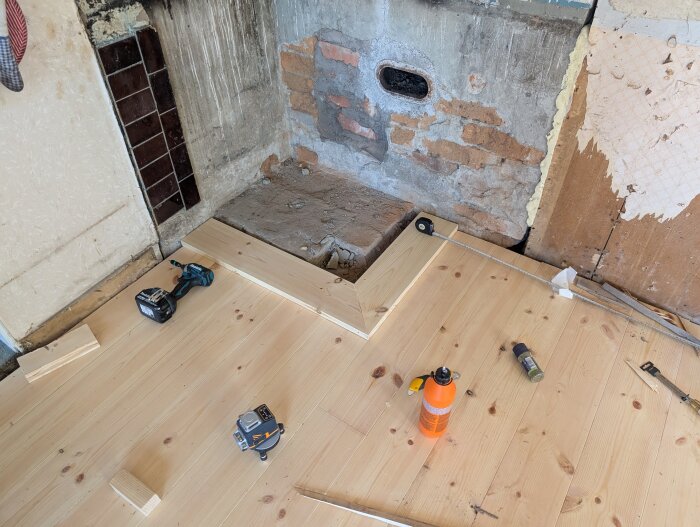 Nylagt trägolv med verktyg på golvet, en borrmaskin och mätinstrument; omgivande väggar visar murverk och gammal puts.