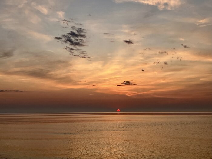 Solnedgång över ett stilla hav med orange och rosa moln på himlen. Solen är halvvägs ner vid horisonten.
