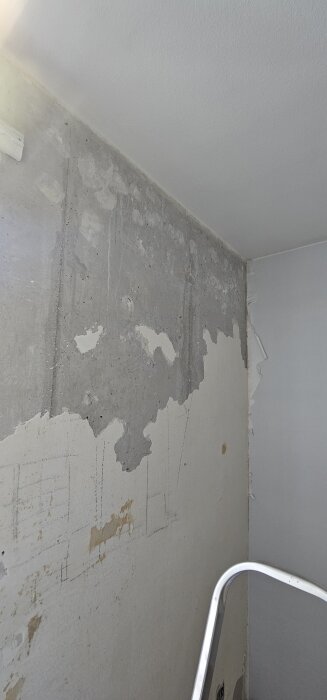 Vägg under renovering med delvis borttagen puts, visar blottat betongfundament. En stege står i rummet.