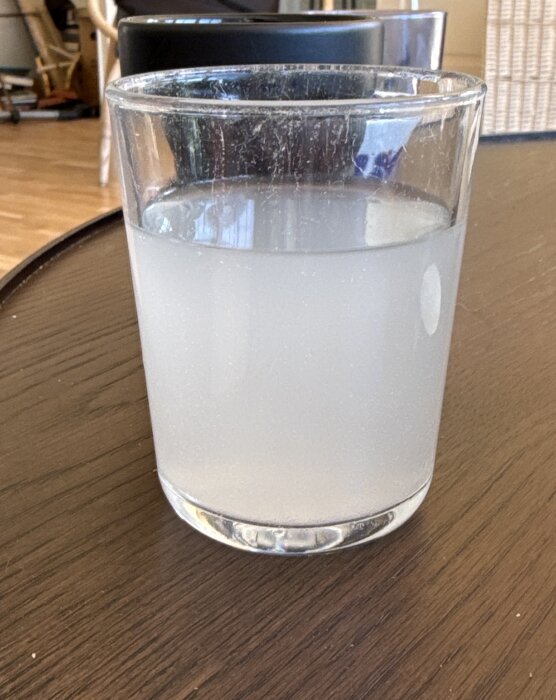 Ett glas med mjölkigt vatten från en borrad brunn, står på ett träbord inomhus.