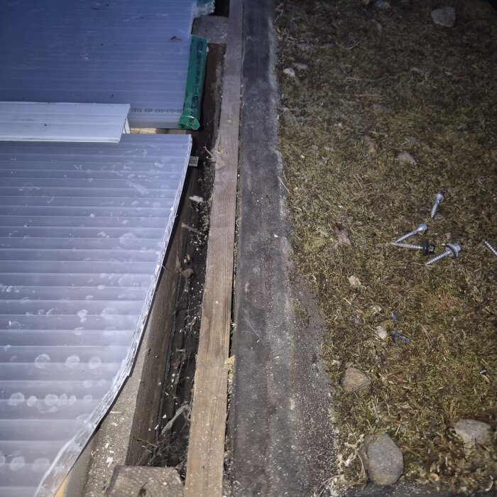 Takplåtar och kanalplast ses bredvid varandra, omgiven av skruvar och träreglar på grästerräng. Handlar om byggprojekt för tätning.