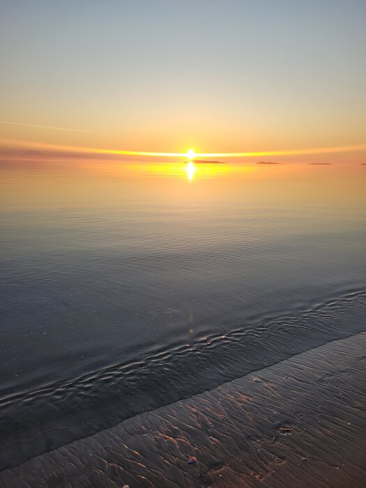 Solnedgång vid Langsanden i Norge strax efter midnatt, med reflektion i havet och sandstrand i förgrunden.