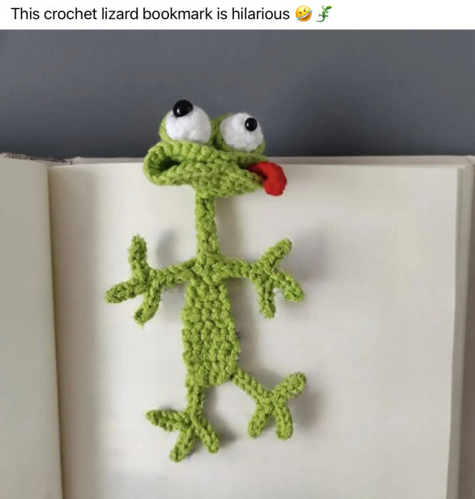 Virkat bokmärke i form av en grön ödla med stora ögon och röd tunga, som ligger i en öppen bok.