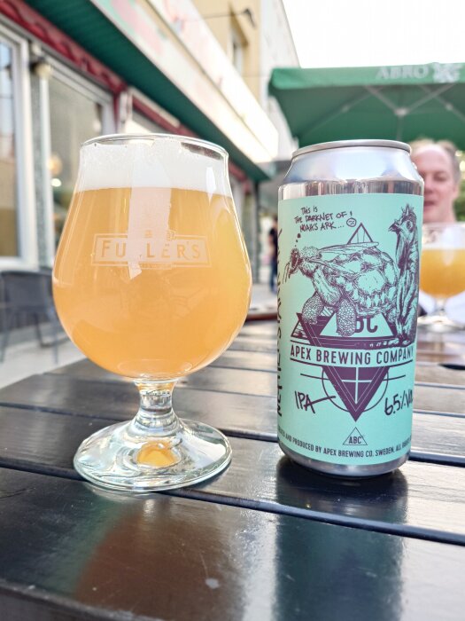 Ett glas öl och en burk från Apex Brewing Company står på ett bord utomhus i Borlänge.