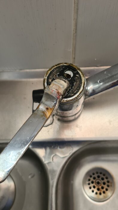 Sliten etthandsgreppsblandare över diskbänk, närbild visar korrosion och slitage vid basen.