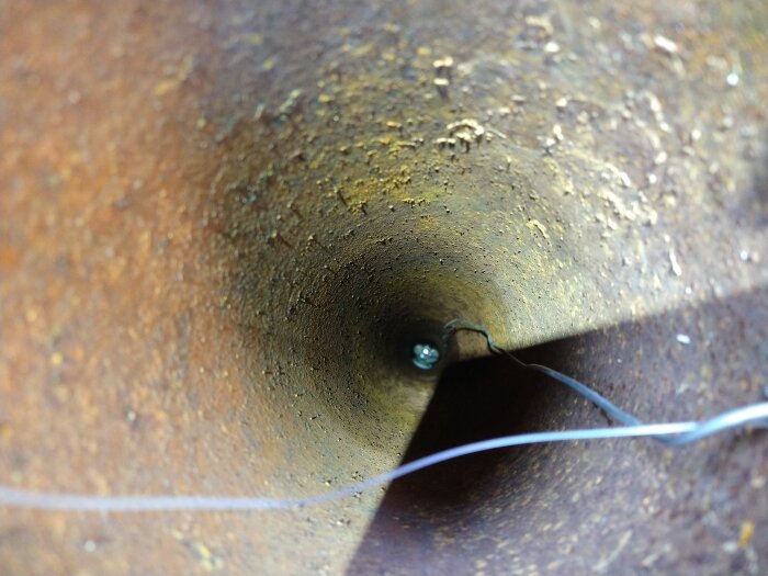 Insida av brunn med trånga väggar och synliga vattenledningar samt en mutter på botten.