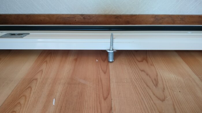 Altandörrens undersida med en karmskruv som ligger ovanpå ett trägolv, i ett projekt där dörren ska installeras bredvid ett fönster.