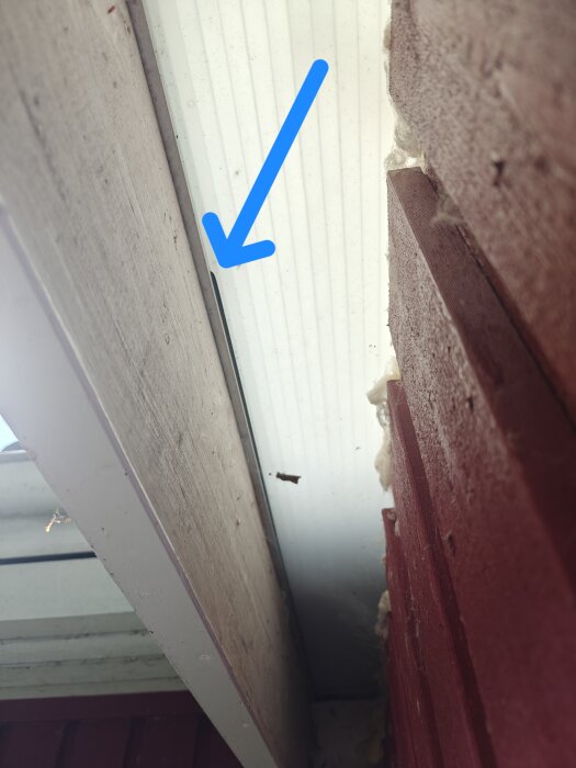 Spricka i taklist markerad med blå pil, nära röd vägg och träpanel.