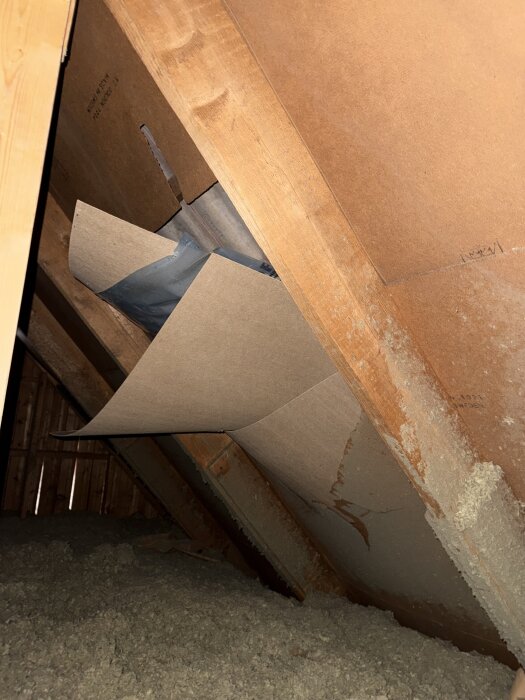 Knäckt masonit på vinden avslöjar bruten folie, inomhus syns isolering och träkonstruktioner. Potentiella stormskador.