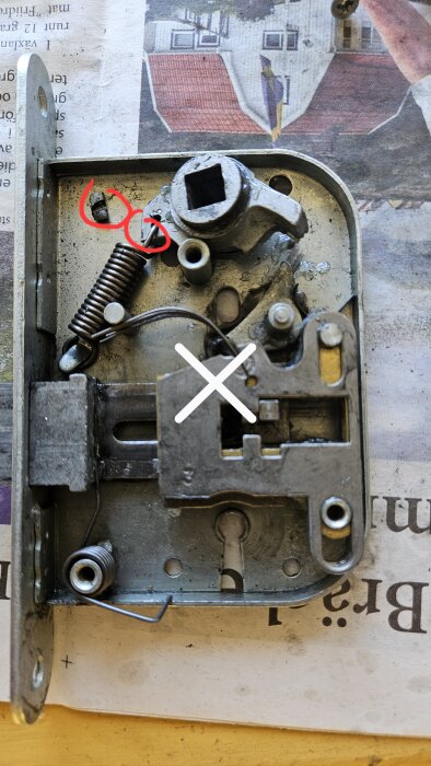 Låsmekanism med fjäder och två röda markeringar, där en del har flyttats för att reparera ett Boda-lås från en matkällardörr.