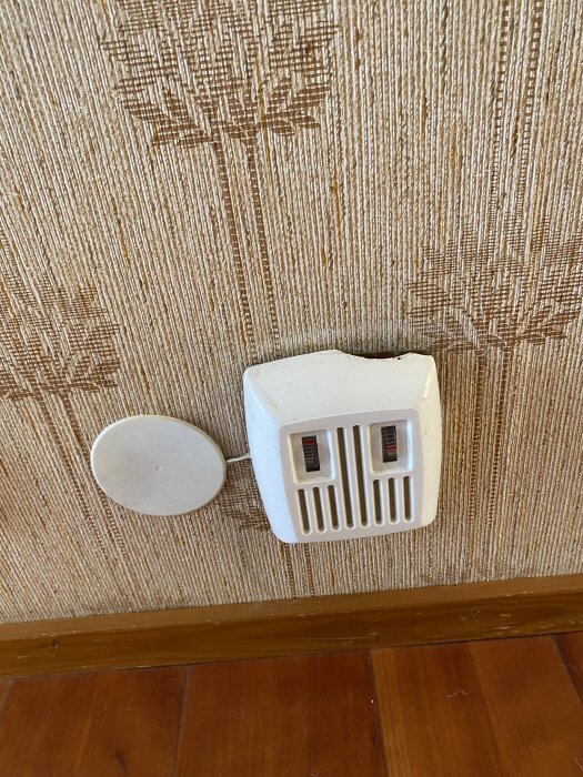 Gammal ringklocka monterad på en vägg med mönstrad tapet i ett hus från 1960-talet.