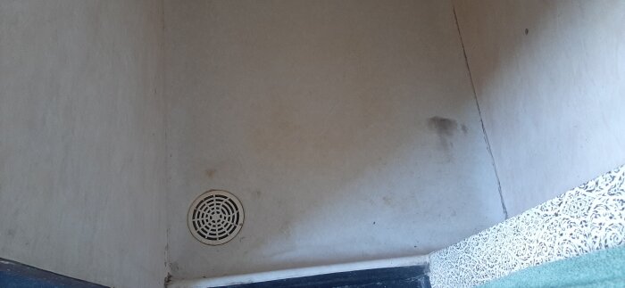 Slitet duschutrymme med våtrumstapet och golvbrunn, antydan till fläckar och slitage på väggarna.