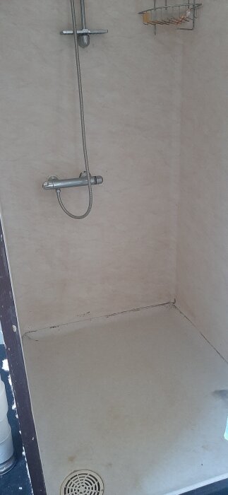 Duschutrymme med äldre våtrumstapet på väggar och golv, duschblandare och avlopp synliga, ytor kan ha märken och slitage.