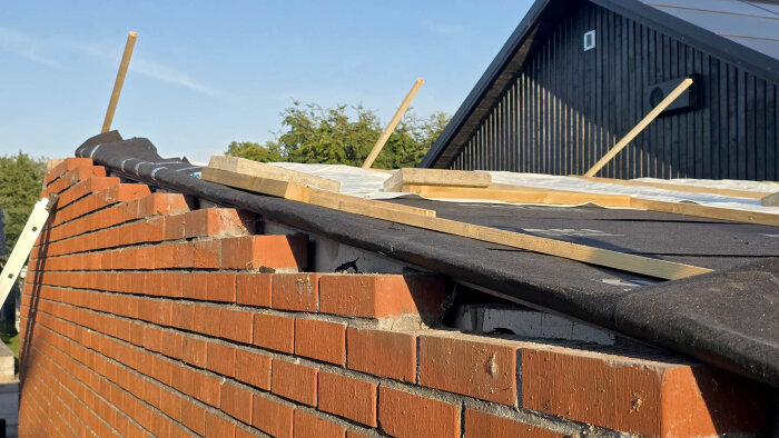 Rött tegelvägg, svart takduk och trälister. Ett projekt med vindskiva i fokus, synliga detaljer av byggprocess ovanpå väggen.