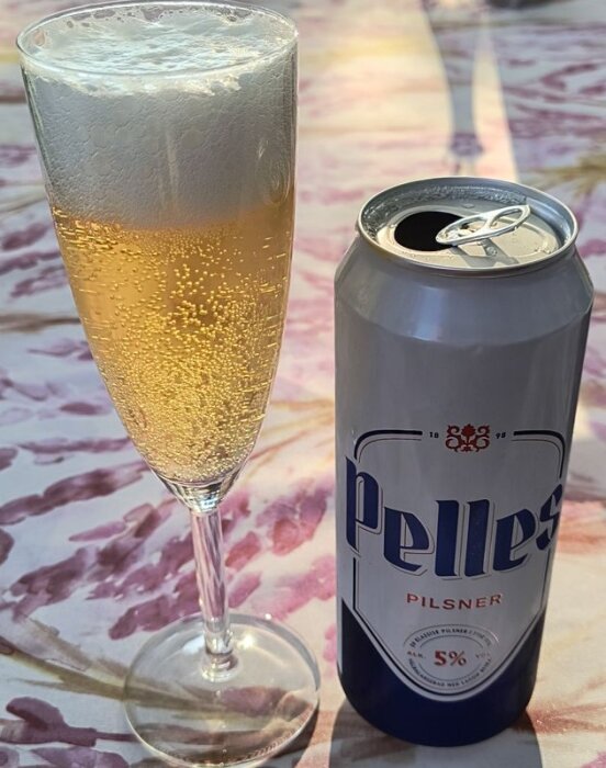 En burk Pelles Pilsner och ett glas öl med skumkrona står på ett blommigt bord.