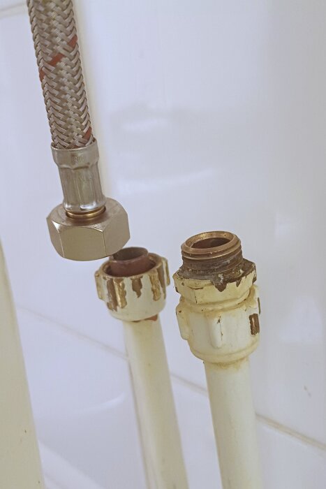 Gamla rör och kopplingar för en toalettblandare där en ny kopplingsdel hänger ovanför, visar problem med passform.