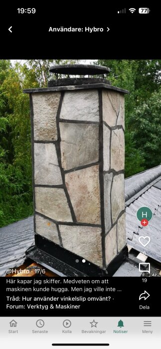 Skorsten klädd med ojämnt mönstrad skiffer, omgiven av grönska, med svart plåtvid basen och en mörk hatt på toppen.