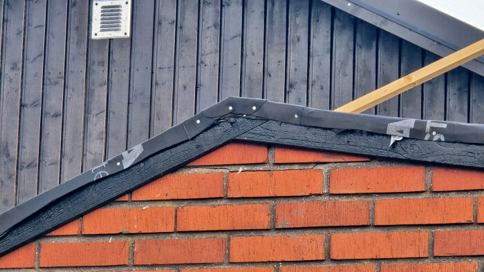 Tegelvägg med svart tak och takduk som ska fästas. Tydlig detaljerad vy av skarvarna och infästningar på vindskivan.