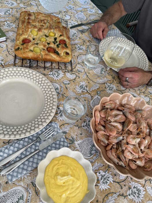 Focaccia med tomater och örter, saffransaioli och grillade räkor på ett dukat bord.