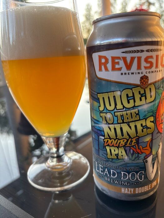Burk av Juiced to the Nines Double IPA från Revision Brewery bredvid ett glas med öl, fotat i solnedgången.
