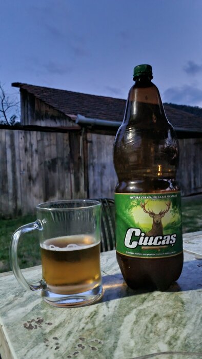 Ölglas och 2,25l PET-flaska med öl på bord utomhus vid skymning, etikett med hjort.